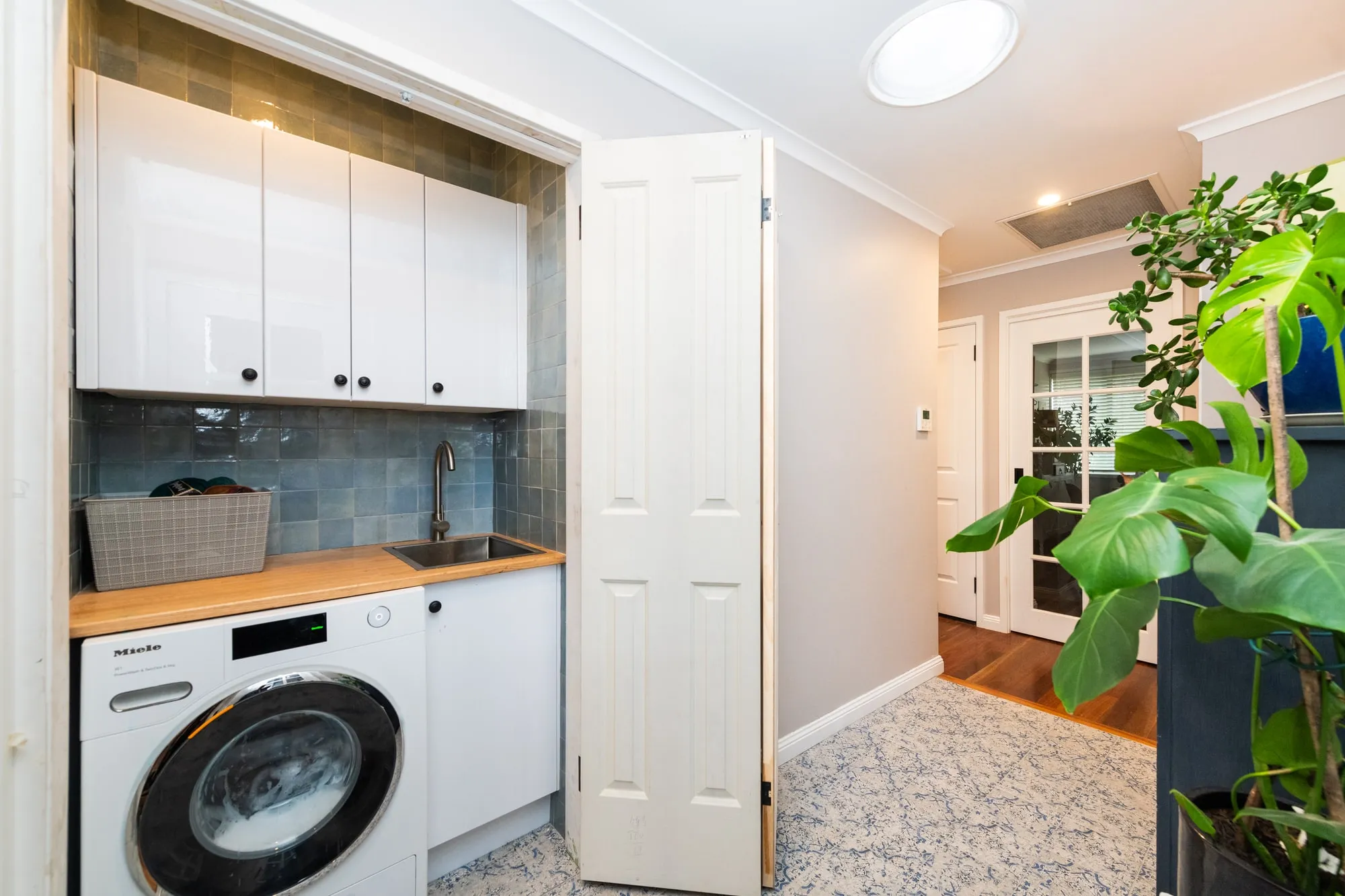 Euro-style laundry with white cupboards, blue splashback tiles and bifold doors