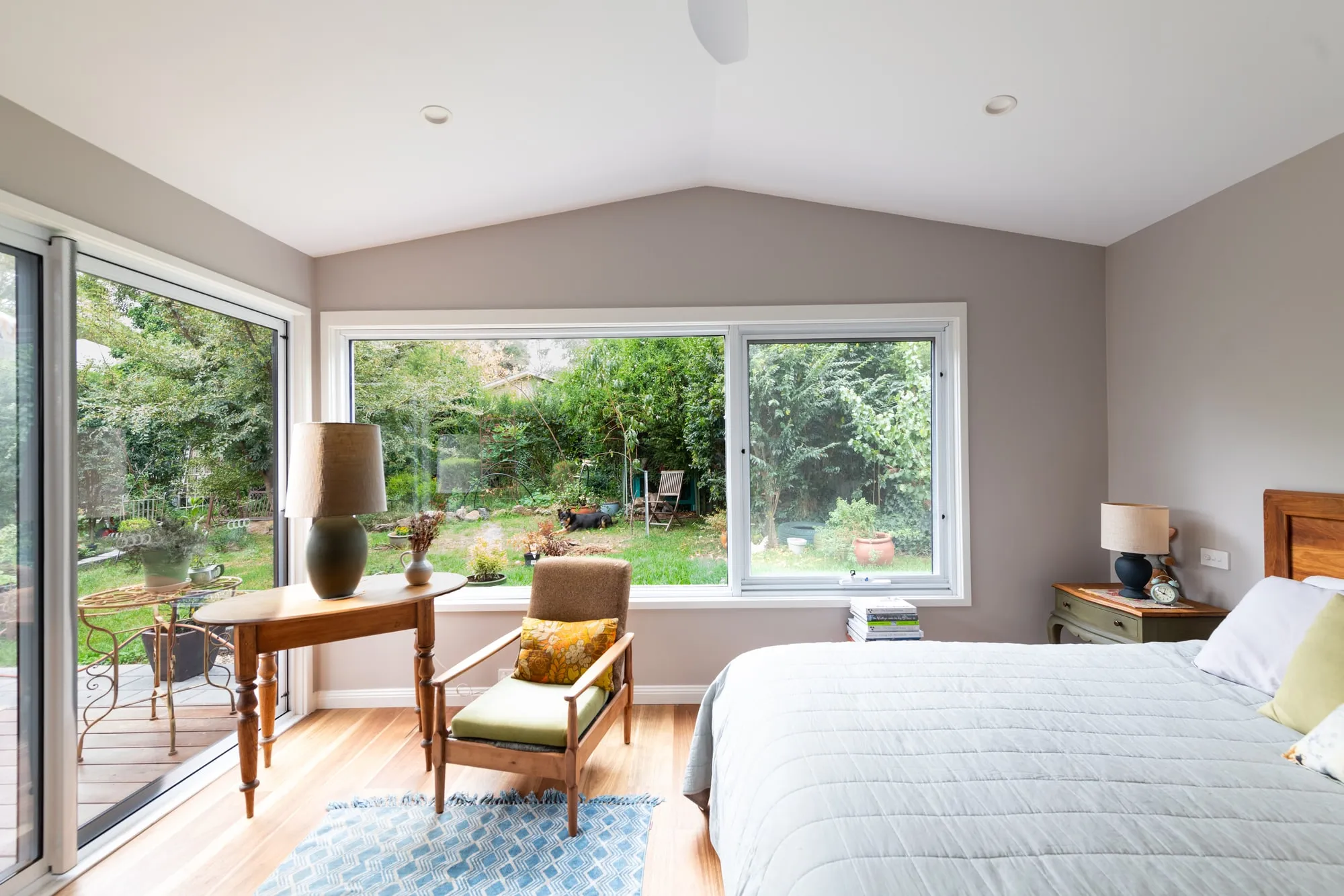 Master bedroom with large windows looking out to a leafy green garden