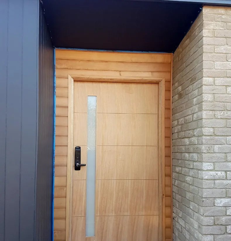 New timber front door with a long glass panel, between dark cladding and pale brick