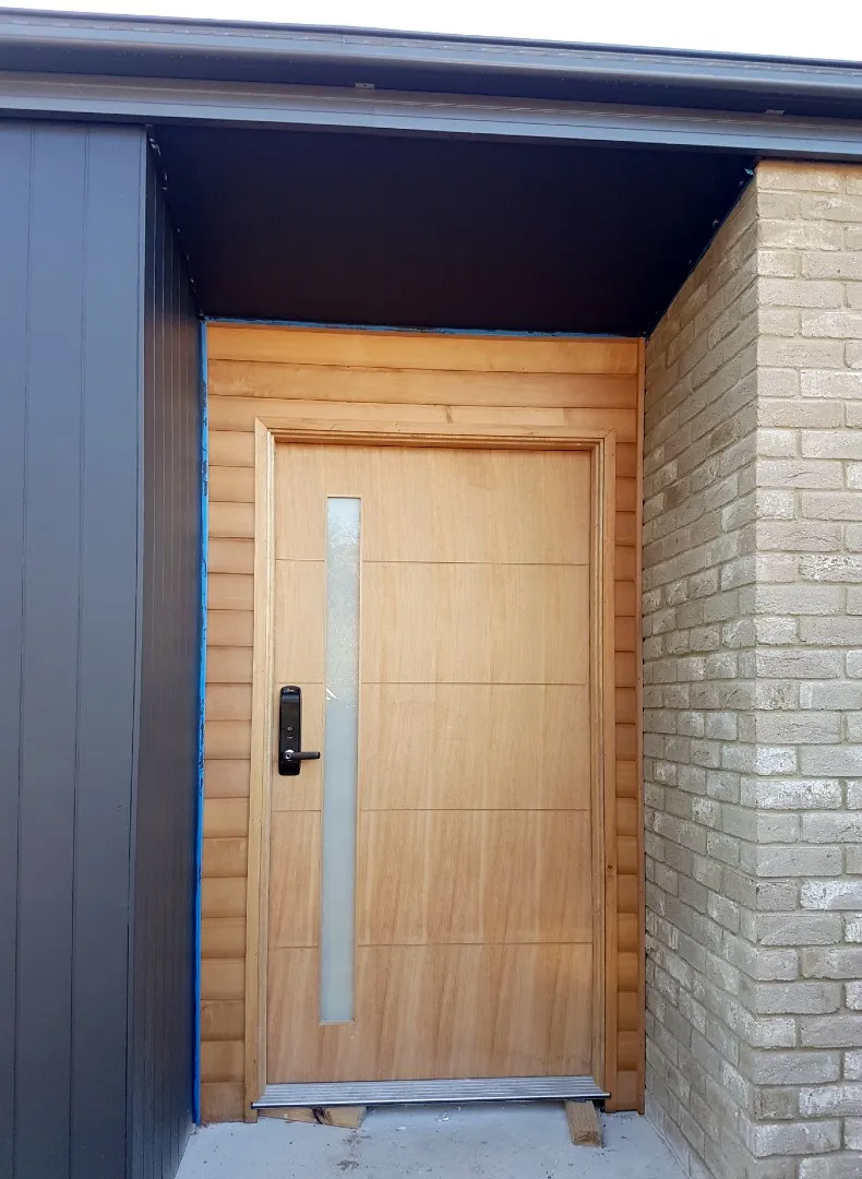New timber front door with a long glass panel, between dark cladding and pale brick
