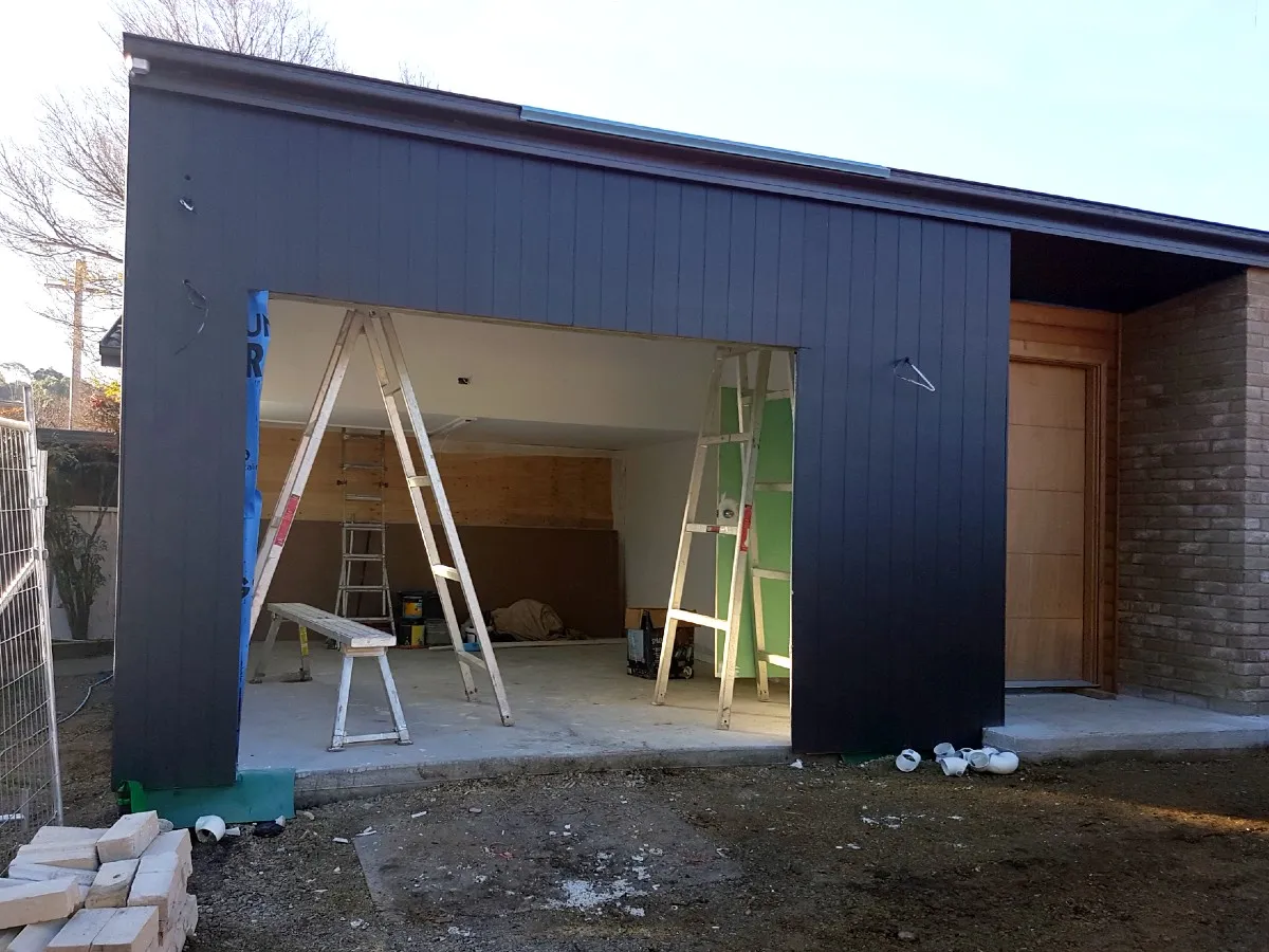 Dark clad extension under construction with a large opening and ladders inside