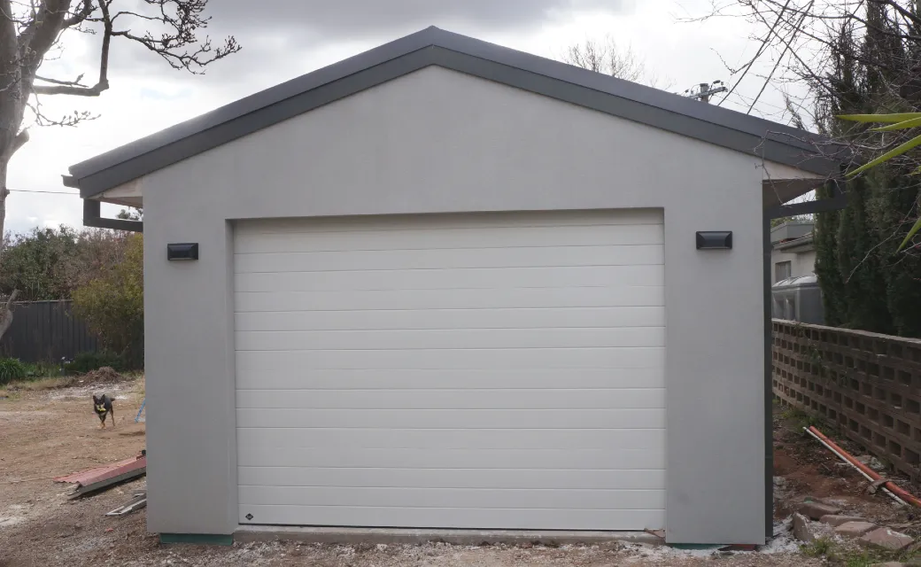Front of newly build garage featuring light gray render and off-white roller door