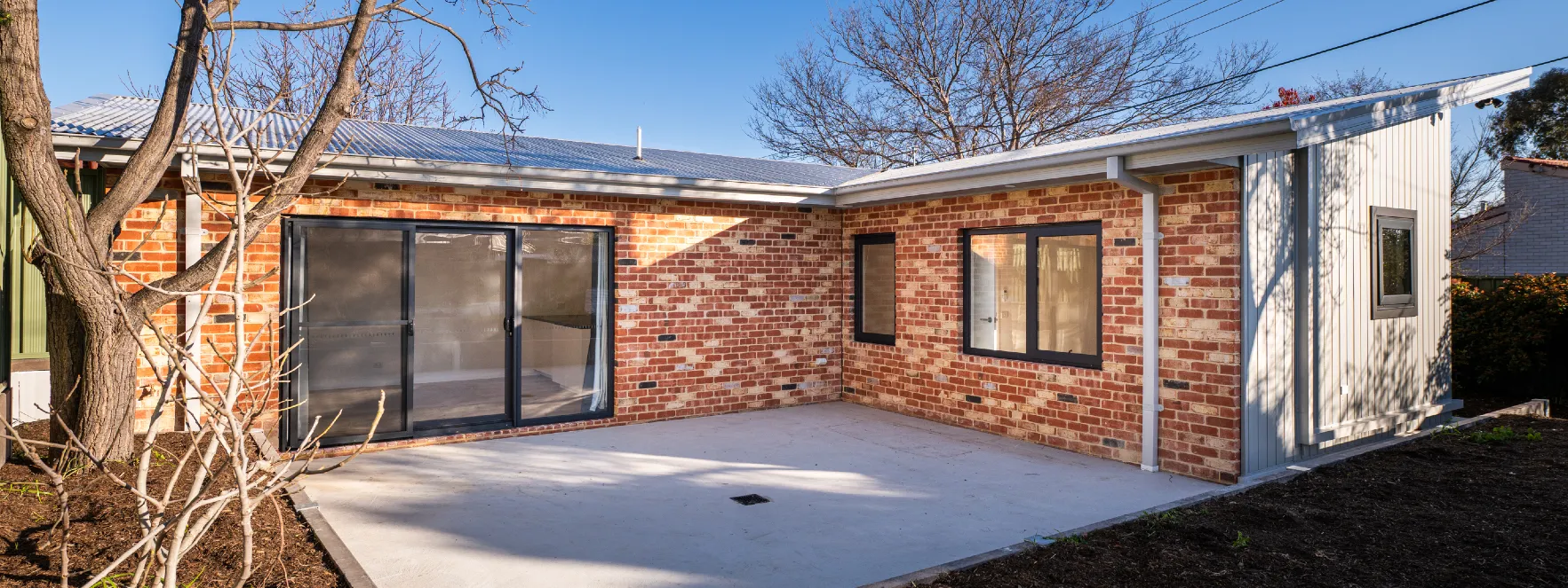 Exterior of newly completed 2 bedroom house. Show feature wall recycled bricks and large alfresco area