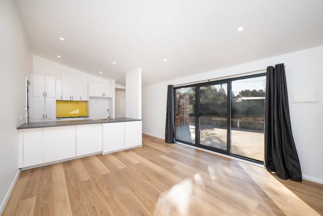 Looking through the living area towards the kitchen, room features raked ceiling and large glass sliding door