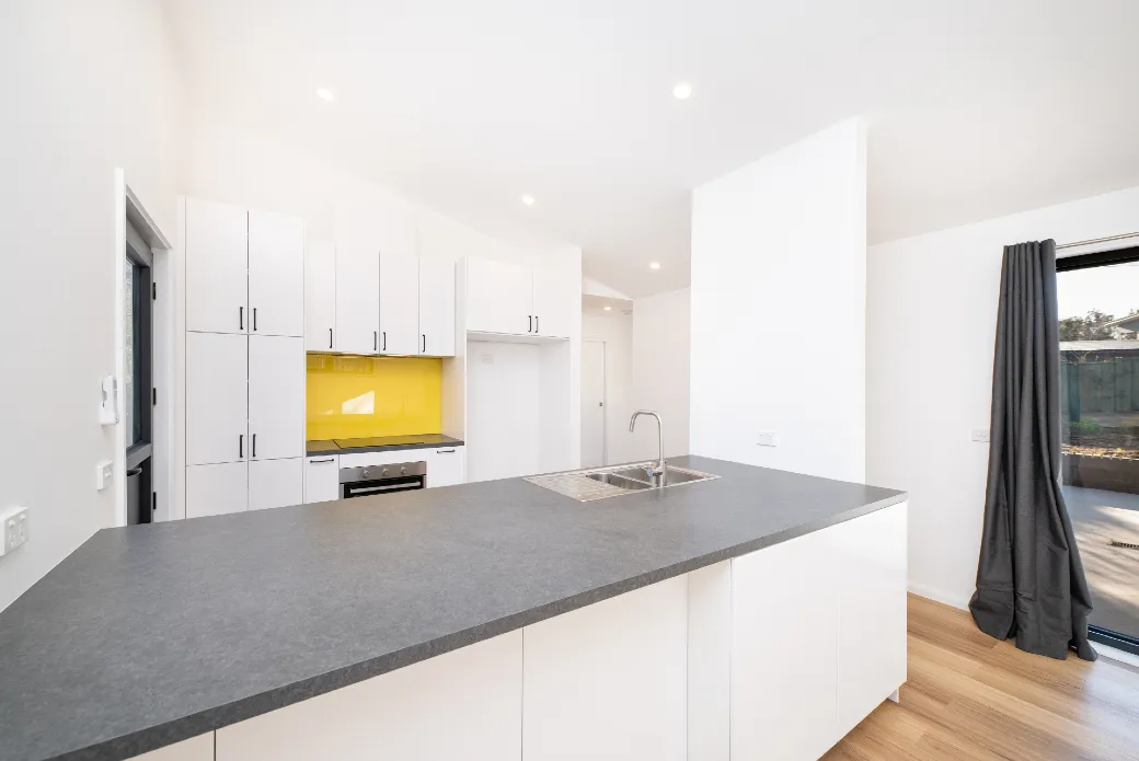 New white kitchen with yellow splashback behind stove, bench space in the foreground
