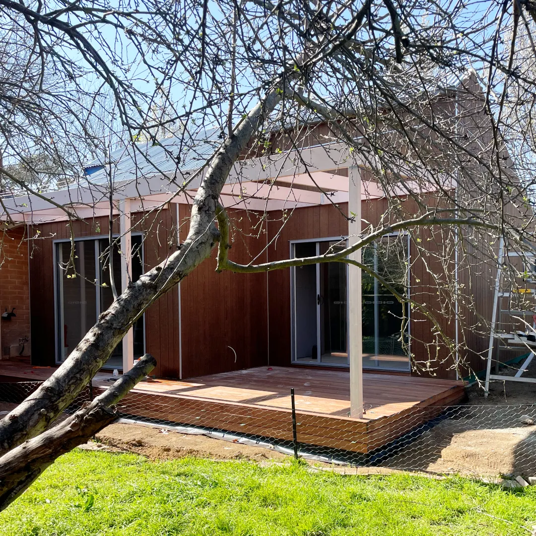 Rear of the extension with timber cladding, sliding doors and a new deck behind a tree