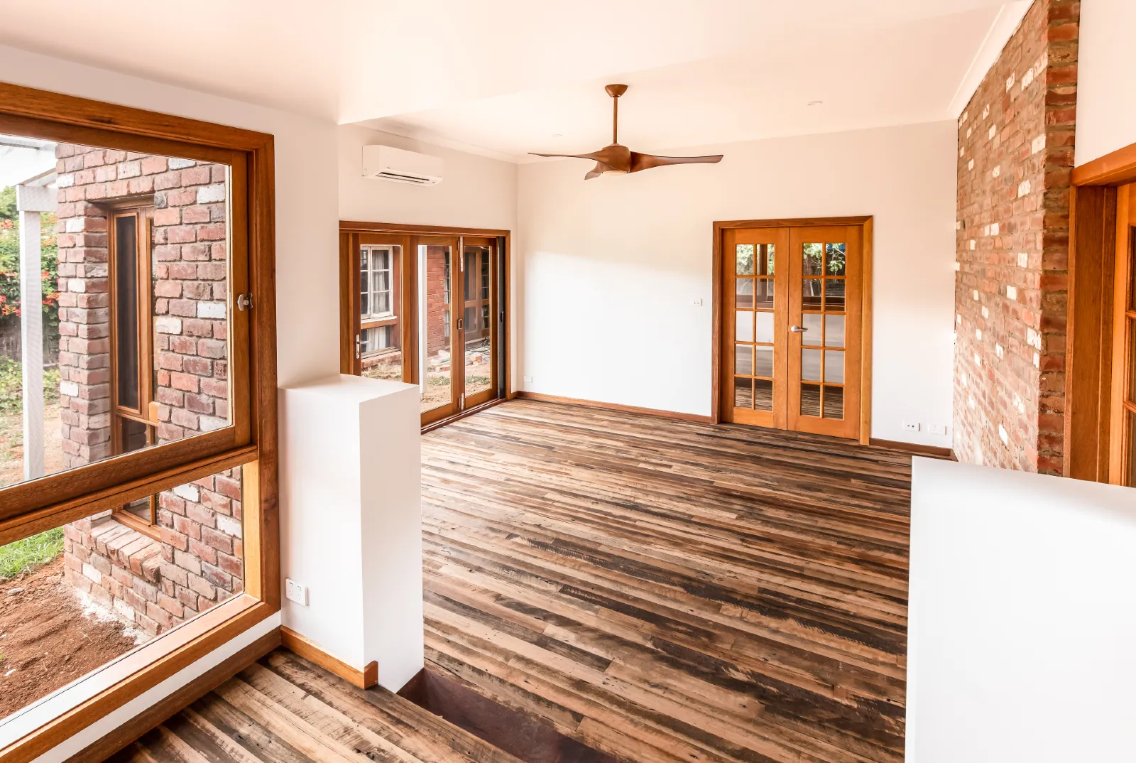 Open living room with timber floors, brick feature wall and timber-framed French doors